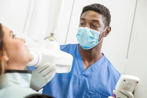 Dental assistant with mask speaking with patient while moving overhead lamp